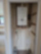 A modern white boiler mounted on a partially finished wall, with visible copper pipes and wiring