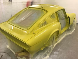 A yellow-painted vintage car partially covered with plastic sheets