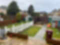 A back garden with a white picket fence, green lawn, garden sheds, and a play area