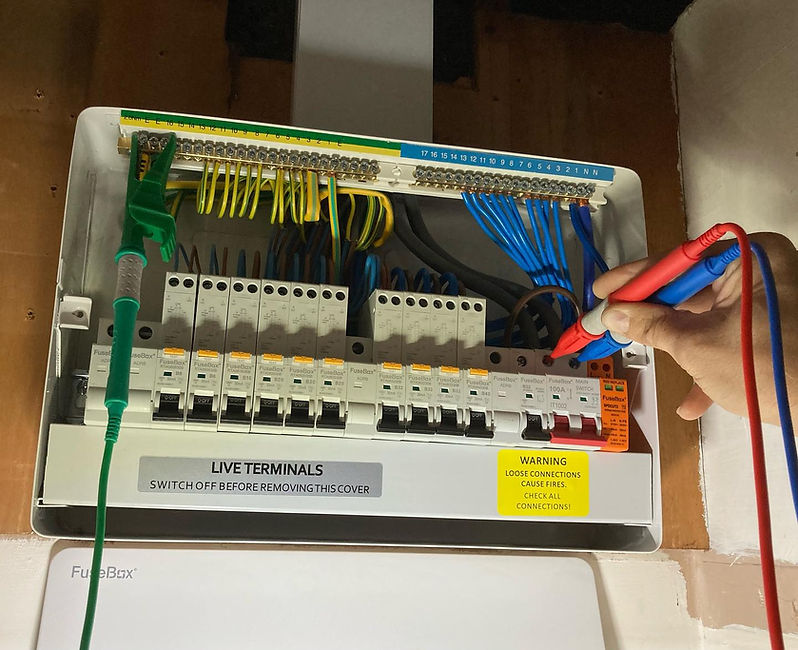 A technician checks terminals in an electrical fuse box using a multimeter with red and black probes