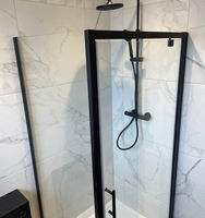 Modern shower enclosure with black frame, glass panels, and a showerhead against a marble tiled wall
