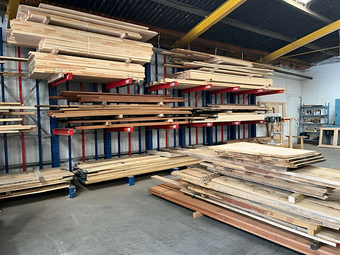 Stacked wooden planks of varying colours and thicknesses are neatly arranged on a shelving in a warehouse