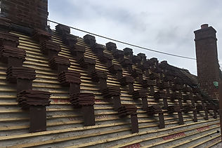 Rooftop with stacked brown tiles on wooden battens, partially completed under a cloudy sky