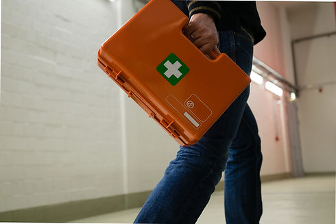 A person walks down a hallway, carrying an orange first aid kit with a green cross