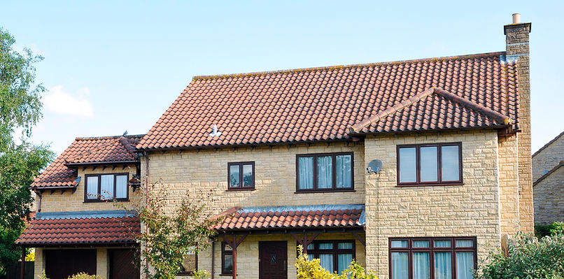 A two-story house with beige brick walls and red tiled roof under a clear blue sky