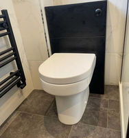 A white toilet installed beside a sleek black wall panel, with tiled flooring