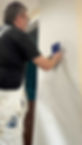 A person applies wallpaper using a smoothing tool on a light-coloured wall
