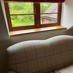 An interior with a plaid sofa back facing a wooden-framed window