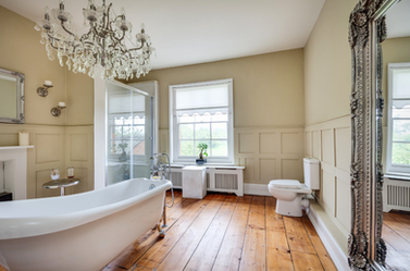 Period style bathroom with a roll-top bath, crystal chandelier, wood flooring, and traditional panelling