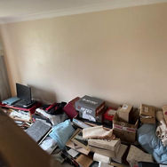 Cluttered room with stacked boxes, papers, and items against the wall