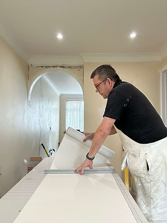 A person is unrolling wallpaper in a light-coloured room