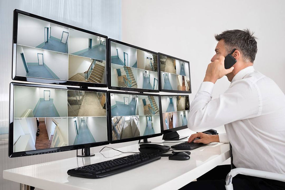 Man in white shirt monitors multiple CCTV feeds on six screens, showing various empty building