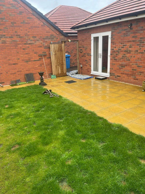 A red-bricked house with a patio with a green lawn and a tiled patio