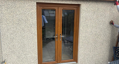 A set of glass French doors with a wooden frame is set in a pebble dash wall