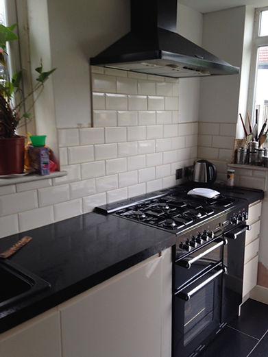 Kitchen counter with black gas range cooker, black extractor hood, cream bevelled subway tiles, and dark worktops.