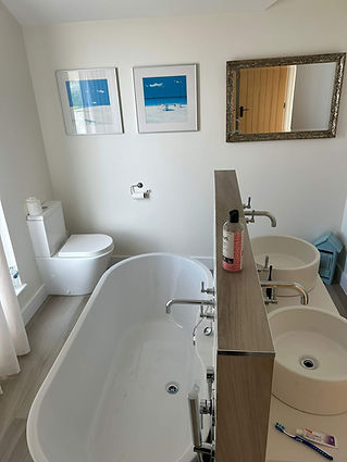 A bathroom with a white freestanding tub, double sinks with chrome faucets, a wall mirror,