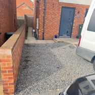 Narrow gravel path beside a brick house, leading to a blue door