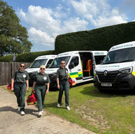 Three paramedics in green uniforms walking past white ambulances with red medical bags