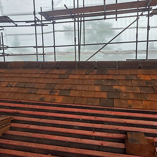 View of a partially constructed roof with reddish-brown tiles, supported by wooden battens