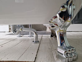 Under-side of white roll top bath featuring chrome p-trap waste pipework and decorative claw feet