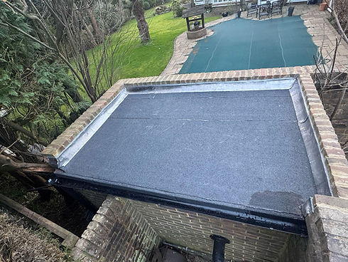 A flat rooftop with a fresh asphalt surface, bordered by a brick wall