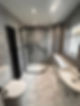 A bathroom with a curved glass shower, sleek black fixtures, a white sink, and marble-patterned tiles