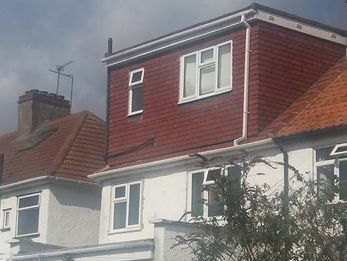 A house with a white lower structure and a red upper story against a cloudy sky