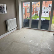 An empty room with a bare concrete floor, a radiator on the left, and large glass doors leading to a garden