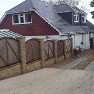 A house with a red brick facade, surrounded by a wood fence and a gravel pathway