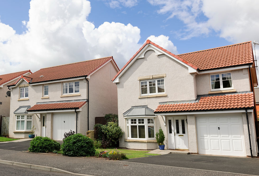 Two modern suburban houses with red-tiled roofs, white walls, and front gardens, set against a cloudy blue sky