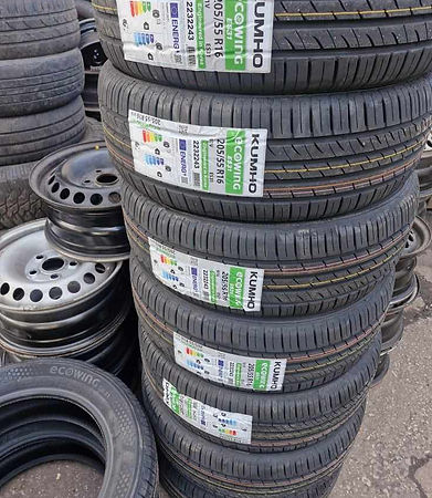 A stack of tyres labelled with details, next to various steel and alloy wheels