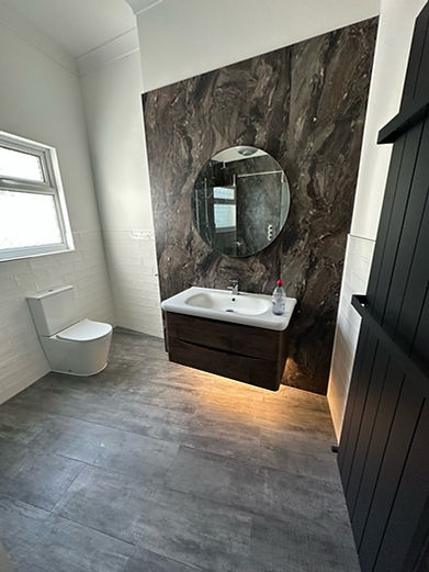 Modern bathroom with dark marble accent wall, floating vanity with under-lighting, round mirror, toilet, and black radiator.