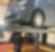 A mechanic works beneath a lifted grey car in a garage