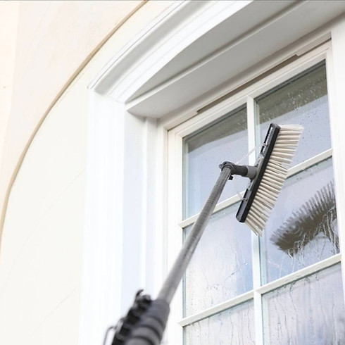 A long-handled brush cleaning a tall window with divided panes