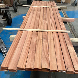 A stack of long, smooth wooden planks arranged neatly on a blue and grey surface in a workshop