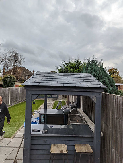 Finished grey slate roof of a garden gazebo structure surrounded by green trees under an overcast sky