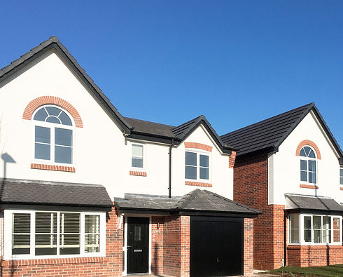 Two modern detached houses with white and red brick facades, dark tiled roofs, and black front doors under a blue sky