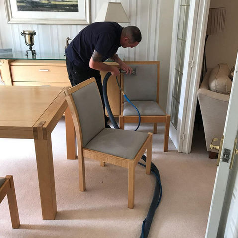 A man is cleaning the dining room chairs.