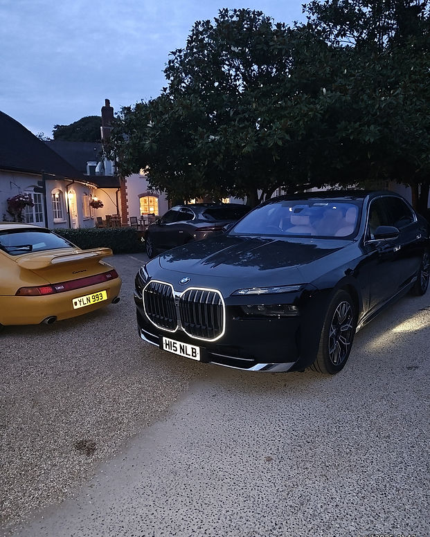 A sleek black BMW sedan with illuminated grille is parked on a driveway beside a yellow Porsche