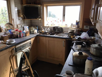Dirty kitchen countertop with utensils and sink full of soiled dishes.