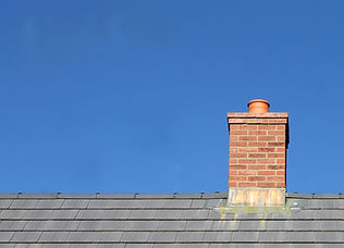Grey tile roof and chimney on house with blue sky background