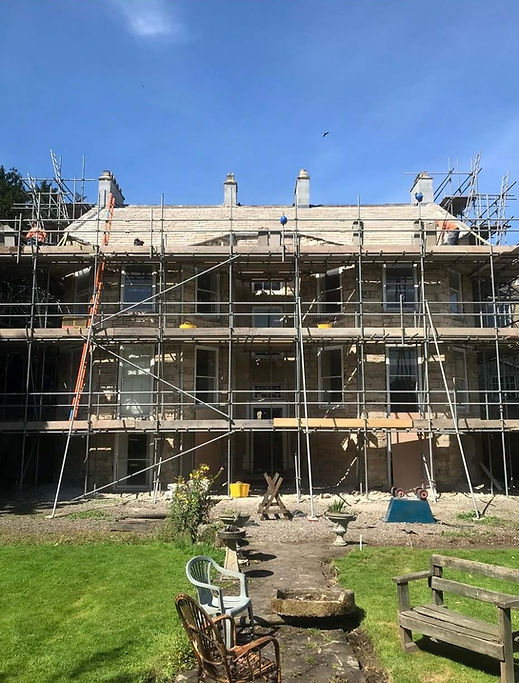 Large stone house undergoing roof restoration with scaffolding installed