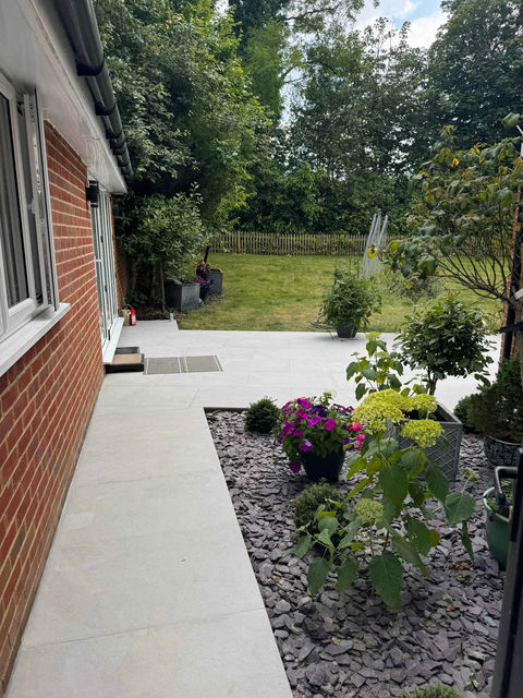 A garden with a narrow patio, green lawn, and flowering plants