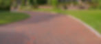A curved block paved driveway bordered by neatly trimmed hedges and colourful flower beds