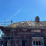 Red brick house undergoing a loft conversion with extensive external scaffolding and roof timbers exposed