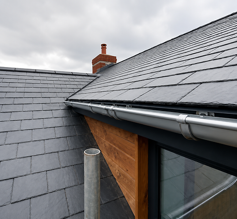Close-up of a modern slate roof with metal guttering, wood panelling, and brick chimney un