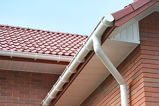 Red-tiled roof with white gutters and downspout on a brick house under a clear blue sky