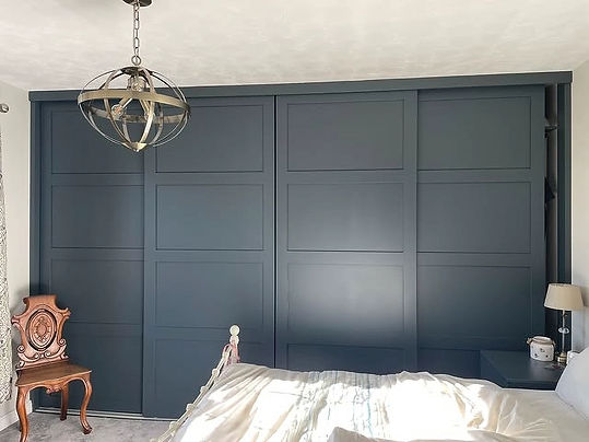 Dark navy blue panelled fitted wardrobe wall stretching behind a dressed double bed