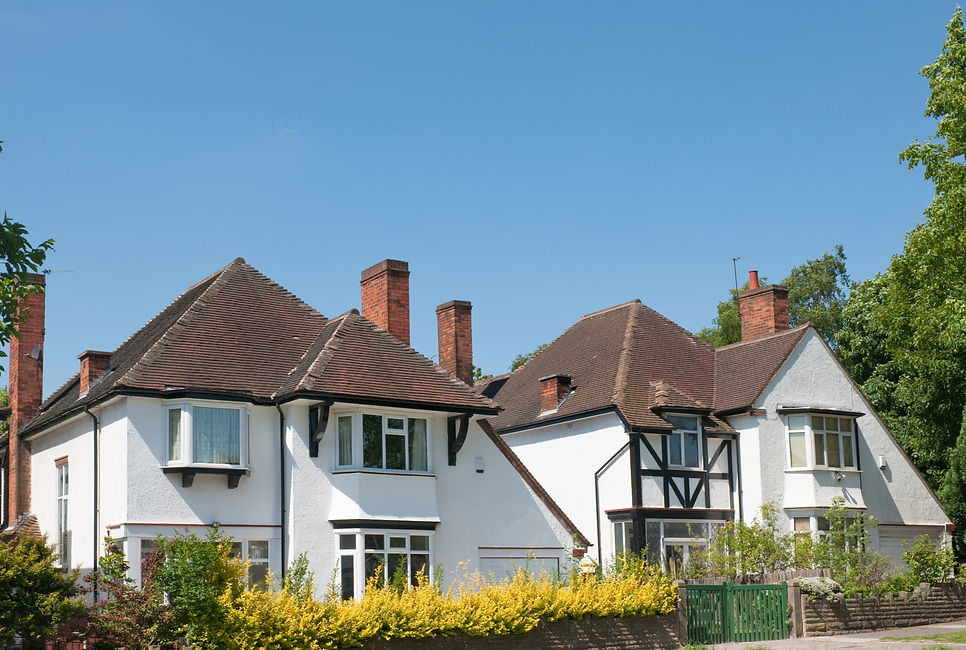 Two large, white semi-detached houses with brown tiled roofs and brick chimneys under a clear blue sky