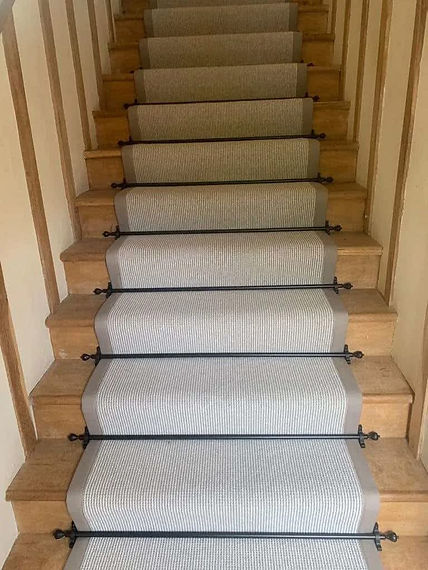 Wooden staircase fitted with a classic striped grey carpet runner secured by black metal stair rods
